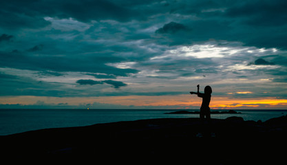 Silhouette woman workout in the morning at stone beach with beautiful sunrise sky. Fit woman stretching body before workout. Exercise for healthy lifestyle. Out door workout. Nature landscape. Freedom