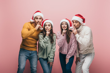 happy friends in sweaters and santa hats showing silence symbols, isolated on pink