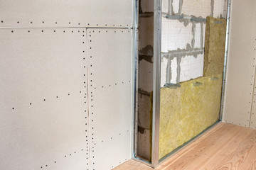 Wall of a room under renovation with mineral rock wool insulation and metal frame prepared for drywall plates.