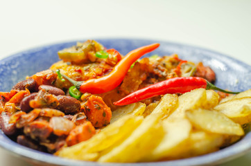 Chicken breast fillet with a chilli and cheese tomato sauce with crispy potato slices and minty bean salad on a blue plate