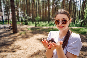 teen girl in round sunglasses collects fallen cones in a city park