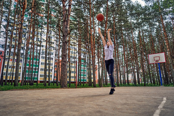 teen girl hipster throws the ball into the basket on a basketball court in a city park