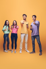 Fototapeta premium smiling friends holding coffee to go and showing thumbs up, on yellow