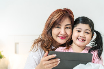 Portrait of two generations of women looking camera. Cute little girl hug granny enjoy time at home, smiling, using tablet computer at home. Happy lifestyle concept.