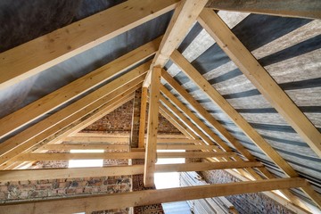 Attic of a building under construction with wooden beams of a roof structure and brick walls.