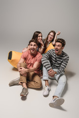 laughing friends sitting on bin bag chair together, on grey