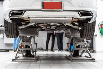 Back side of Car lifted in automobile service and Asian mechanic Checking and torch tire in maintainance service center which is a part of showroom,technician or professional work for customer concept