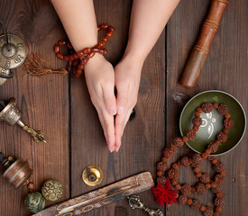 two hands in a prayer pose on a wooden brown table in the middle of vintage Tibetan meditation tools