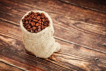 Coffee beans closeup in burlap bag on wooden background.