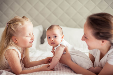 Young beautiful mother holds a baby. Little sister kisses her little sister. Baby. Children bedroom.