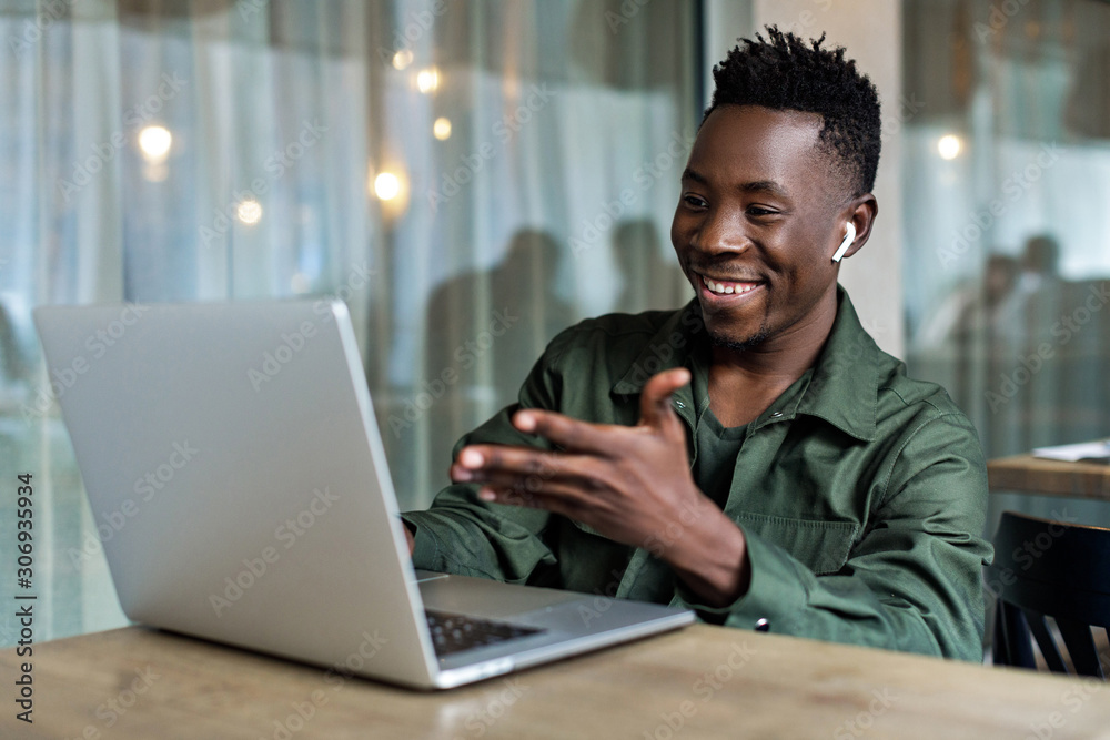 Wall mural handsome african american man using computer and smiling. online video chat with friends