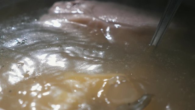 Metallic spoon stirring ukha, a traditional Ukrainian fish soup, boiling in pot  