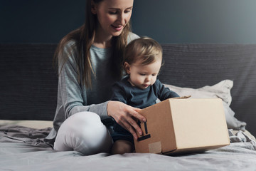 Mother and child sitting on bed and unwrapping package. Family shopping online with quick delivery of goods to your front door. Mailing of order, free shipment using post service. High quality product