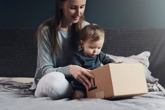 Mother And Child Sitting On Bed And Unwrapping Package. Family Shopping Online With Quick Delivery Of Goods To Your Front Door. Mailing Of Order, Free Shipment Using Post Service. High Quality Product