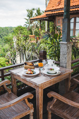 Breakfast with balinese fruit plate, basket with croissants and fruit salad on wooden table on outdoor terrace