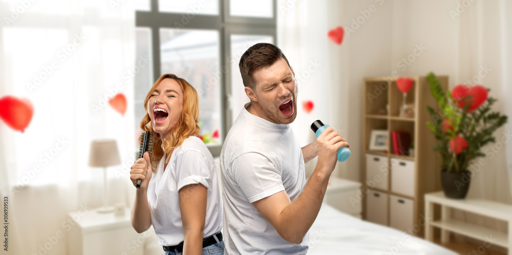 Poster valentine's day, fun and people concept - portrait of happy couple in white t-shirts couple singing to hairbrush and lotion bottle over home bedroom decorated with heart shaped balloons background