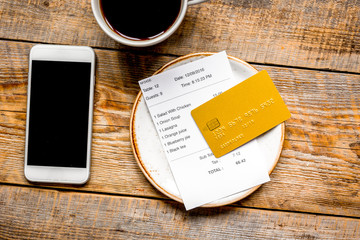 credit card for paying, mobile and check on cafe wooden desk background top view mock up