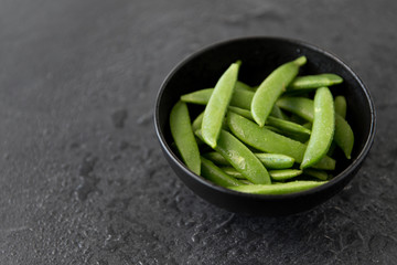 vegetable, food and culinary concept - close up of peas in bowl on wet slate stone background
