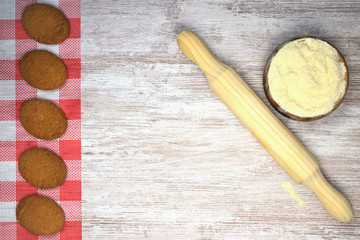 Rodillo amasador , junto bol de madera con harina y galletas horneadas sobre pequeño mantel