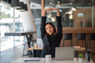 Business women or working lady are stretch oneself or lazily for relaxation on her desk while doing...