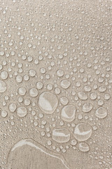 Texture of water drops on fabric textile close-up. Rain background in beige color. Waterproof surface abstract. 