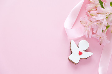 Cookies in the shape of an angel with a pink ribbon with lisianthuses on a pink background.