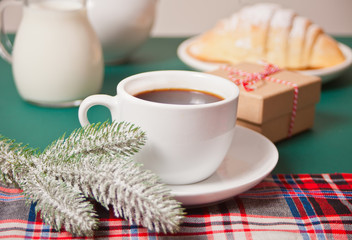 Cup of tea, homemade bun croissant, Christmas gift box and Christmas pine branch on the green background