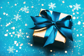 Attractive gift with blue ribbon on a blue background. Snow and lights. Merry Christmas, New Year, winter concept.