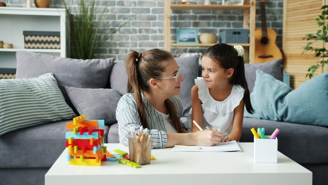 Mother and adorable little daughter are drawing together at home talking bonding at table in house. Childhood, leisure activities and people concept.