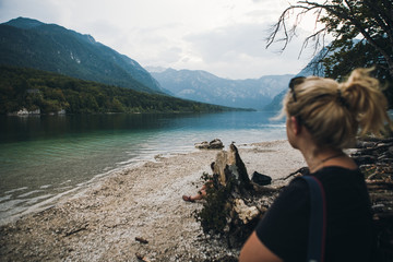 Young woman in the coast. Tourist in the foreground. Wild mountain lake with clean water. Wild and green mountains in the background. Selective focus. girl in foreground in defocus.