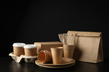 Eco - friendly dishware and paper bag on black background, space for text