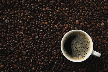 Cup of coffee on coffee beans background, top view
