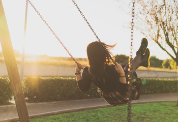 Girl having fun on the swing - young millenial woman relaxes in the park - concept of freedom and well-being - warm color with sunny golden light - obrazy, fototapety, plakaty