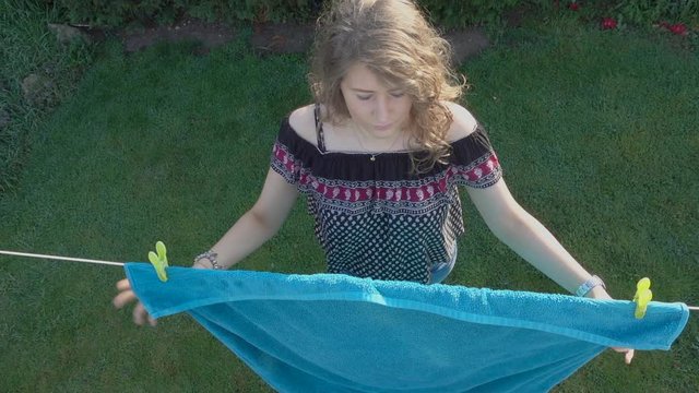 Slow motion POV overhead shot of a beautful young woman pegging a damp towel onto a garden / yard washing line, in the early morning sunshine.