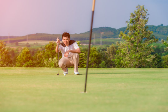 Asian male golfer kneeling holding golf club and checking path line
