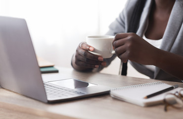 Fototapeta na wymiar Unrecognizable black businesswoman drinking coffee and using laptop in office