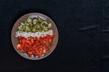 Simple salad of cucumbers and tomatoes with sour cream flavored with salt and black pepper on a dark background