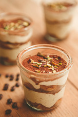 Tiramisu with pistachios and coffee in jars on a wooden countertop