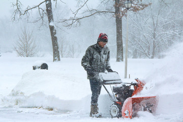 Senior caucasian man snow blowing during blizzard using ear protectition