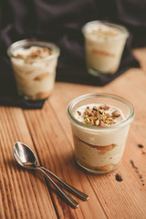 Tiramisu with pistachios and coffee in jars on a wooden countertop
