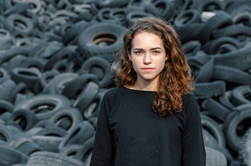 Fototapeta na wymiar Beautiful girl, curly hair, portrait on the background of a dump of old car tires. Looking at camera.