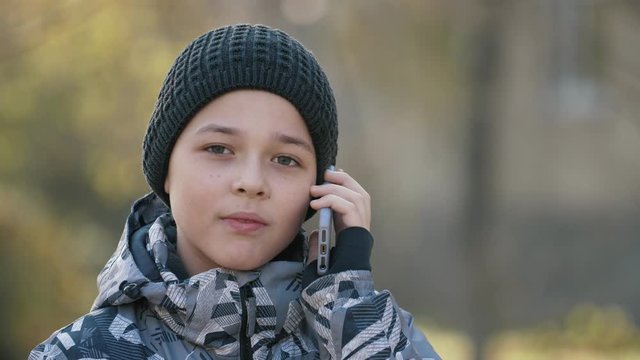 Cheery child in a knitted hat talking with his grampa on a phone in a park in autumn  