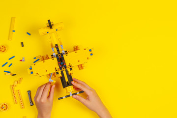 Child hands making construction plane over yellow background. Robotic, learning, technology, stem...