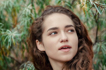 Portrait of a girl with brown curly hair on a background of green bush.