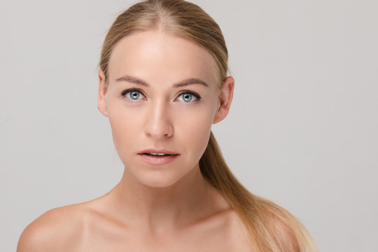 Portrait of beautiful young blonde with natural makeup looking aside and posing on white isolated background. Naked female model without accessories in studio. Concept of beauty and tenderness.