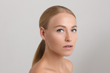 Studio portrait of attractive blonde caucasian woman with blue eyes and bare shoulders over white background. She is looking at camera with eyes wide open. Pure, smooth and flawless skin concept.
