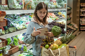 A young woman with a notebook buys groceries in the supermarket.