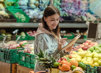 A young woman with a notebook buys groceries in the supermarket.