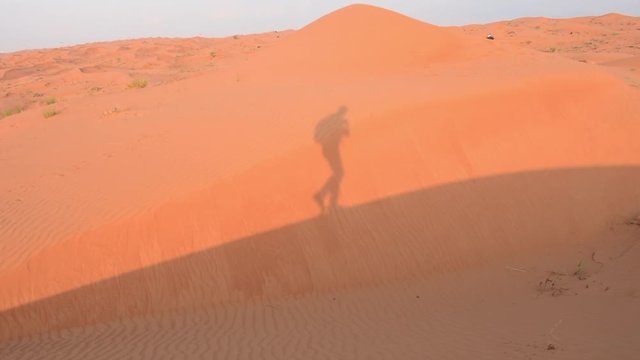 Shadow of hiker or walker up the orange evening colored sand dunes in Ras al Khaimah, United Arab Emirates near Dubai.