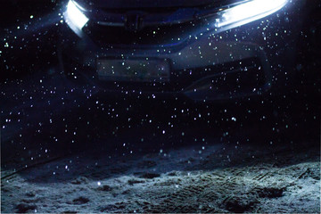 snowflakes during snowfall lit with light from car headlights at night on a road